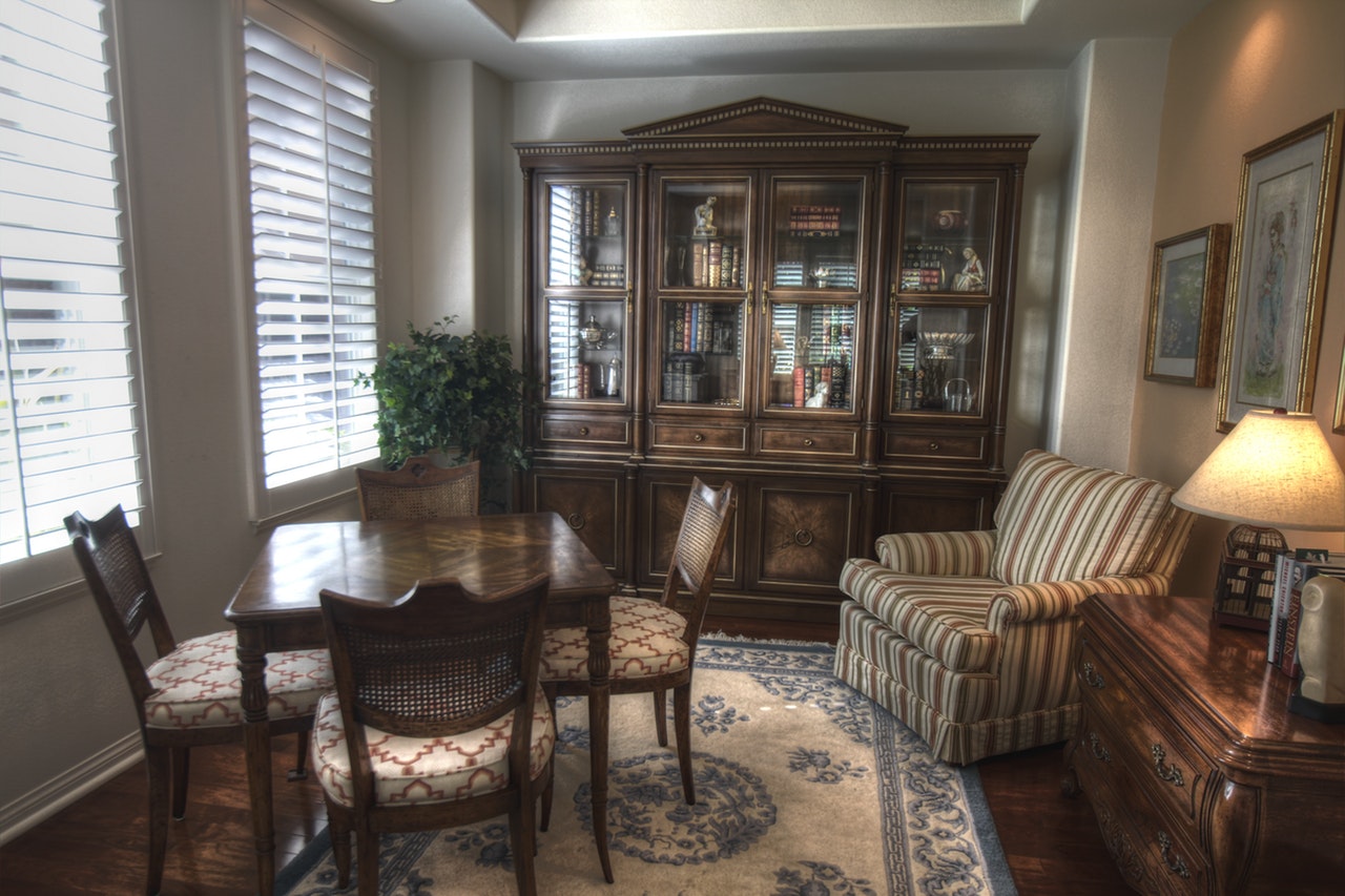 a living room with an earth tone style with wooden chairs, tables, and a bookshelf